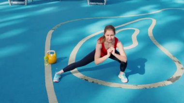 Bir atlet sokak sporları sahasında gerinir. Genç bayan sporcu antrenman yapıyor, bir su ısıtıcıyla antrenman yapıyor.