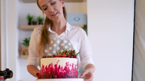 Kochen und Dekorieren von Kuchen mit Sahne. Junge Konditorin in der Küche dekoriert roten Samtkuchen — Stockvideo