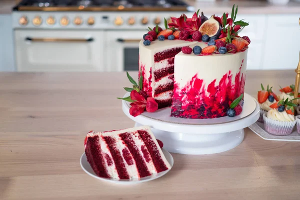 Μεγάλο όμορφο κόκκινο βελούδινο κέικ, με λουλούδια και μούρα στην κορυφή. Φέτα σε ένα πιάτο, επιδόρπιο. — Φωτογραφία Αρχείου