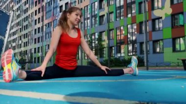 Bir atlet sokak sporları sahasında gerinir. Genç bayan sporcu antrenman yapıyor, bir su ısıtıcıyla antrenman yapıyor.