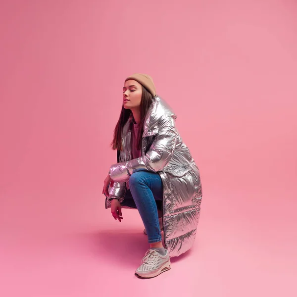 Elegante mujer joven de moda y moderna en una chaqueta hinchada luz abajo. La chaqueta es un color metálico plateado. — Foto de Stock