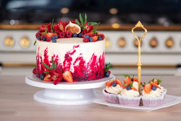 Μεγάλο όμορφο κόκκινο βελούδινο κέικ, με λουλούδια και μούρα στην κορυφή. Νόστιμα γλυκά μάφιν με κρέμα γάλακτος, — Φωτογραφία Αρχείου