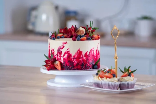 Μεγάλο όμορφο κόκκινο βελούδινο κέικ, με λουλούδια και μούρα στην κορυφή. Νόστιμα γλυκά μάφιν με κρέμα γάλακτος, — Φωτογραφία Αρχείου