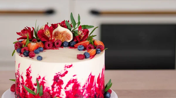 Μεγάλο όμορφο κόκκινο βελούδινο κέικ, με λουλούδια και μούρα στην κορυφή. Επιδόρπιο στο τραπέζι της κουζίνας. — Φωτογραφία Αρχείου