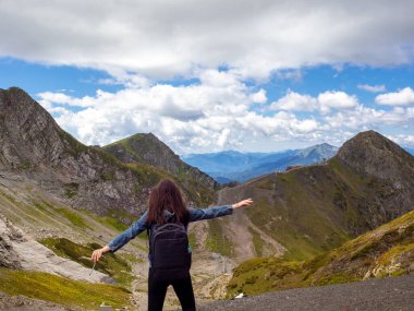Bir dağ panoramasının arka planında genç bir bayan turist. Kollarını açarak ayakta duruyor.,
