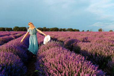 Lavanta tarlasında yürüyen şapkalı mutlu ve güzel bir kadın.