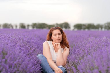 Düşünceli bir kadın lavanta tarlasında oturmuş manzaranın ve kokunun tadını çıkarıyor.