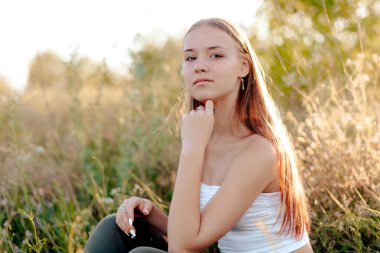 Parkta, batan güneşin altında neşeli genç bir kadın uzaklara bakıyor.