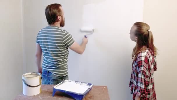 英俊的父亲正在向他的女儿展示如何粉刷墙壁 幸福的家庭 男人和青少年女孩一起做修理在家里 爸爸和孩子画墙在平白色 使用滚子 — 图库视频影像