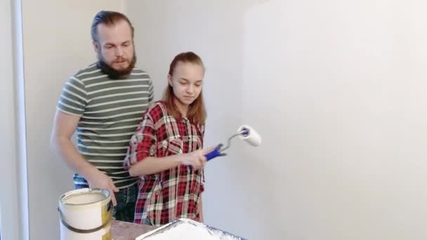 ハンサムな父親は 彼の娘を見せている塗装する方法 幸せな家族の男とティーンの女の子一緒に自宅の修理を行います お父さんと子供絵画壁 白のフラット ローラーを使用して — ストック動画