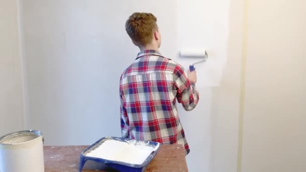 后视图青少年男孩绘画内部墙壁在平面使用油漆辊 英俊的少年自己在他的房间里做修理 油漆墙 家居装修或装修概念 — 图库视频影像
