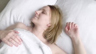 Güzel genç kadın beyaz yastık üzerinde uyuyor. Waking up, germe ve gülümseyen kızdır. Beyaz kadın yatakta Waking up erken sabah sonra.