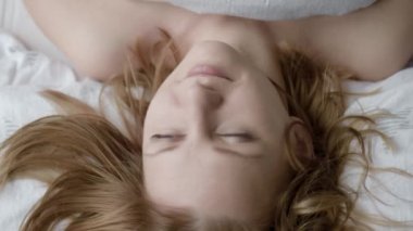 En iyi görünüm güzel genç kadın yüzü. Başını yastığa dinleniyor. Kız onun baş ve Looking kameraya taşır. Güzel beyaz kadın yatakta Waking up erken sabah sonra.