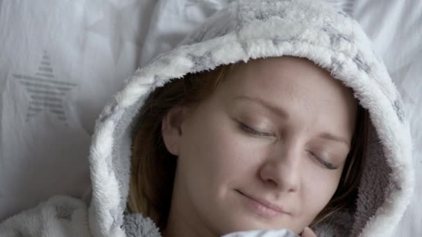 美丽的年轻女子睡在白色的枕头上 女孩醒来 看着相机和微笑 白种人女性穿着睡衣 在清晨醒来后在床上戴着头套 — 图库视频影像