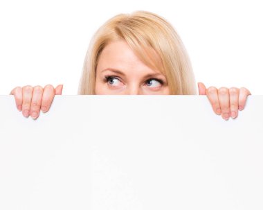 Boş boş tabela boşaltmak ile gösterilen mutlu gülümseyen genç kadın portresi. Beyaz arka plan üzerinde izole büyük beyaz afiş tutarak işkadını.