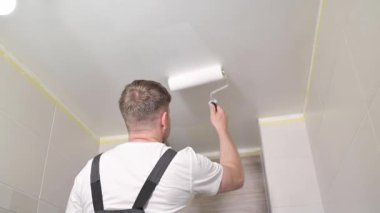 İşçi tavanı beyaz boyayla boyuyor. Boyacı banyo tavanını tekerlekli aletle boyuyor. Boya silindiri kullanan tamirci tipi. Dairenin tamiri. Ev sahibi evde tadilat yapıyor..