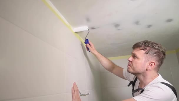 ホワイトペイントで作業者の塗装天井 画家の男性はローラーツールでバスルームの天井をペイント 塗装ローラーを使用してハンディマンタイプ アパートの修理 自宅で改修工事を行う住宅所有者 — ストック動画