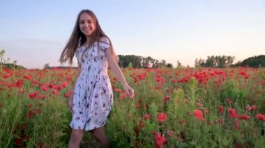 Beyaz elbiseli güzel gülümseyen genç kız gelincik tarlasında koşuyor ve eğleniyor. Mutlu çocuk gün batımında çiçek açan kırmızı haşhaş çayırında oynuyor. Doğada boş zaman.