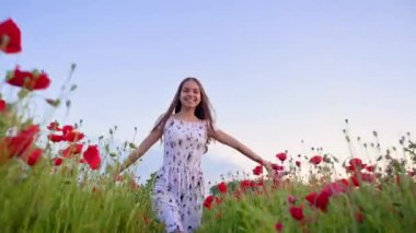 Beyaz elbiseli güzel gülümseyen genç kız gelincik tarlasında koşuyor ve eğleniyor. Mutlu çocuk gün batımında çiçek açan kırmızı haşhaş çayırında oynuyor. Doğada boş zaman.