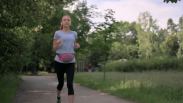 青少年带着耳机听音乐 在公共绿地公园里跑步 累了的女孩停止慢跑 有选择的重点 健康生活方式概念 — 图库视频影像