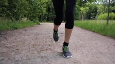 Kız ayaklarının yavaş çekim çekimi yazın parkta koşar. Sağlıklı yaşam tarzı kavramı. Dişi fitness dışarıda koşuyor. Bacaklar ve spor ayakkabılar..