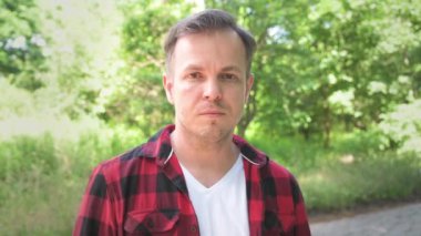 Pozitif adam kameraya gülümser. Başparmak işareti gösteren adam. Yeşil arka planda yetişkin bir erkeğin açık hava portresi.