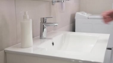 Kadın eli banyoda musluğu lavaboya döker. Akan su. Yetişkin kadın musluğu kapatıyor.