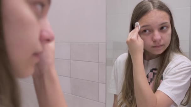 ティーンの女の子はバスルームミラーで彼女の顔を見て 綿のパッドを使用しています 問題の肌を持つ美しいティーンエイジャー 顔の概念上の健康管理 — ストック動画