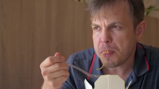 空腹の男のカフェやレストランでのファーストフードを食べているを取る フォークを持つ男は麺アジア料理とフライドポテトを食べる — ストック動画