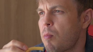 Aç Adam lokantada ya da kafede fast food yiyor. Adam ketçaplı patates kızartması yiyor. - Yakın çekim. Erkek yüzü.