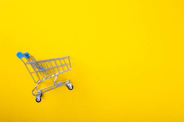 Sarı arka plandaki alışveriş arabasının fotokopi alanı ile yakın plan görüntüsü.