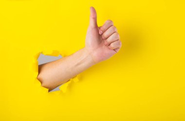 El, sarı kağıtta yırtık bir delikte baş parmak işareti gösteriyor..