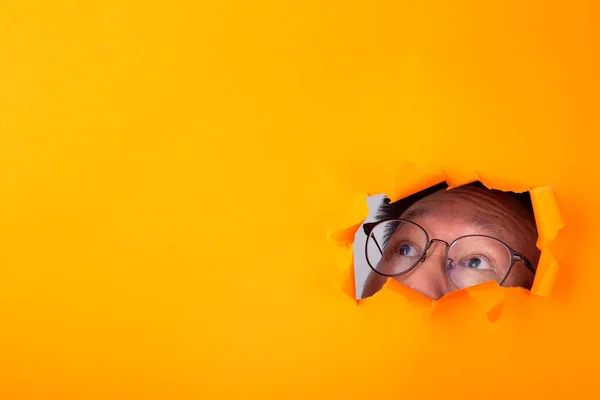 Hombre Con Espectáculo Mira Través Agujero Cortado Fondo Papel Naranja —  Fotos de Stock