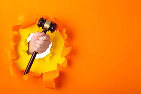 Mano Sosteniendo Mazo Juez Través Una Pared Papel Naranja Rota —  Fotos de Stock