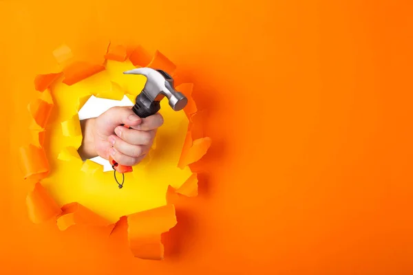 Hand Mit Hammer Durch Zerrissenes Orangefarbenes Papier Baukonzept — Stockfoto