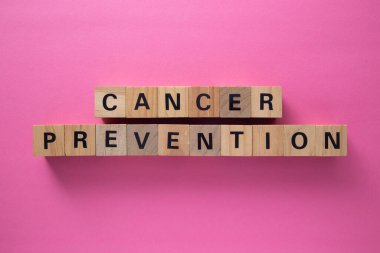 Ahşap bloklar pembe arka planda kanser önleme yazarak farkındalığı ve erken teşhisi teşvik ediyor.