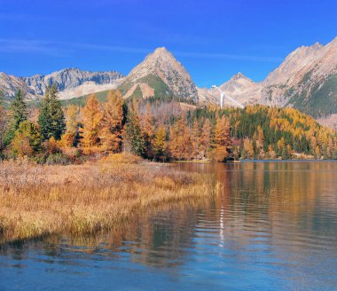 Güneşli sonbahar manzarasında Strbske Pleso tarn suları, High Tatras tepeleri ve arka planda ünlü kayak atlayışları görülüyor. Strbske Pleso Tatras Ulusal Parkı 'na (Tanap) aittir ve High Tatras' ın Slovakya tarafındaki en büyük ikinci buzul gölüdür..