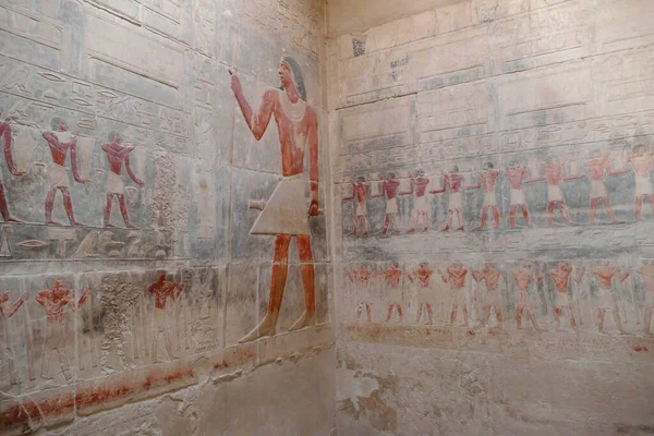 SAQQARA, EGYPT - MAR 11, 2020 - Painted bas relief figures showing daily life in ancient Egypt inside Tomb of Hagmeni, the largest mastaba in the Teti cemetery  in Saqqara, Egypt