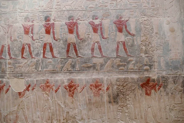 SAQQARA, EGYPT - MAR 11, 2020 - Painted bas relief figures showing daily life in ancient Egypt inside Tomb of Hagmeni, the largest mastaba in the Teti cemetery  in Saqqara, Egypt