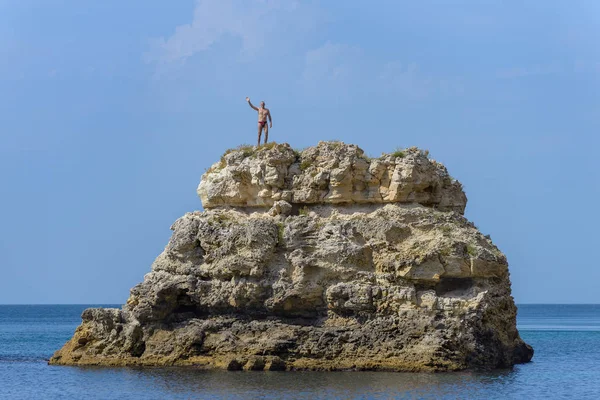 A man in a red swimming trunks stands on top of a cliff