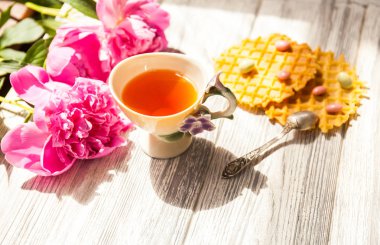 Fincan yeşil çay ve bahar peonies çiçeği waffle ve karamel eski bir ahşap zemin üzerine. Rustik.