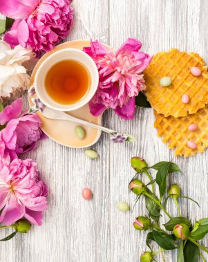 Fincan yeşil çay ve bahar peonies çiçeği waffle ve karamel eski bir ahşap zemin üzerine. Rustik.