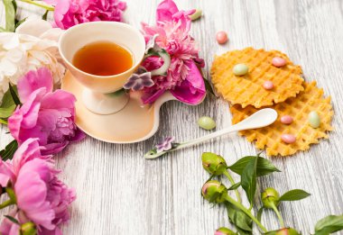 Fincan yeşil çay ve bahar peonies çiçeği waffle ve karamel eski bir ahşap zemin üzerine. Rustik.