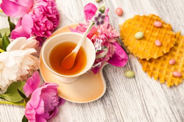 Fincan yeşil çay ve bahar peonies çiçeği waffle ve karamel eski bir ahşap zemin üzerine. Rustik.