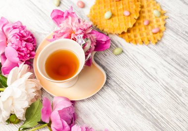 Fincan yeşil çay ve bahar peonies çiçeği waffle ve karamel eski bir ahşap zemin üzerine. Rustik.