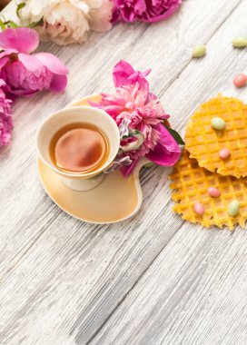 Fincan yeşil çay ve bahar peonies çiçeği waffle ve karamel eski bir ahşap zemin üzerine. Rustik.