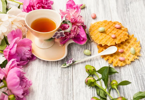 Fincan yeşil çay ve bahar peonies çiçeği waffle ve karamel eski bir ahşap zemin üzerine. Rustik.