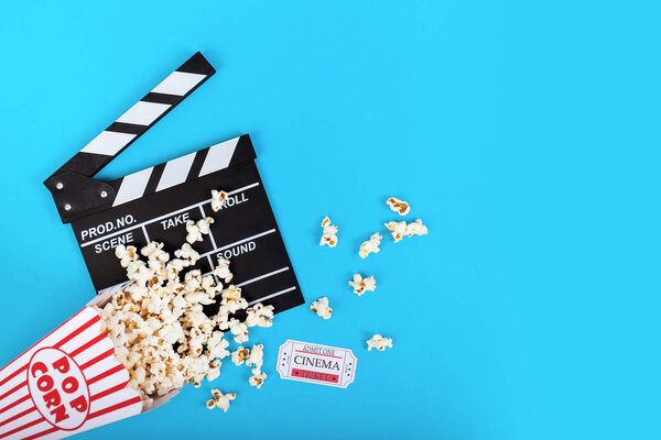 Cinema background. Film watching. Popcorn, ticket and clapperboard on blue background top view copy space