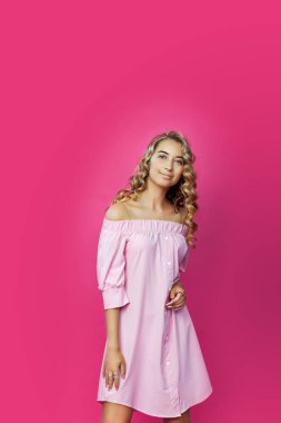 Güzel pembe elbise giyen ve pembe bir arka plan karşı poz uzun kıvırcık saçları oldukça stil sahibi kız. Moda moda stil portre genç mutlu gülümseyen kadın, kopya alanı.