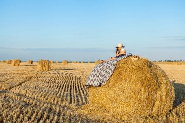 Sevimli kız bir haystack köyü hasır şapka giyiyor süt içip pişmiş mal buğday alanında sıcak ve güneşli yaz akşamı. Sevimli küçük çocuk çavdar alanında günbatımı.
